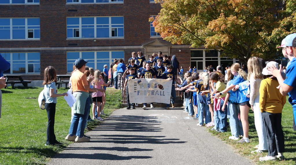 students holding a football banner walking down a path with kids on the side