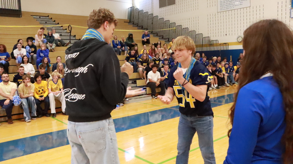 Two students with hands out in front of others sitting in gym bleachers