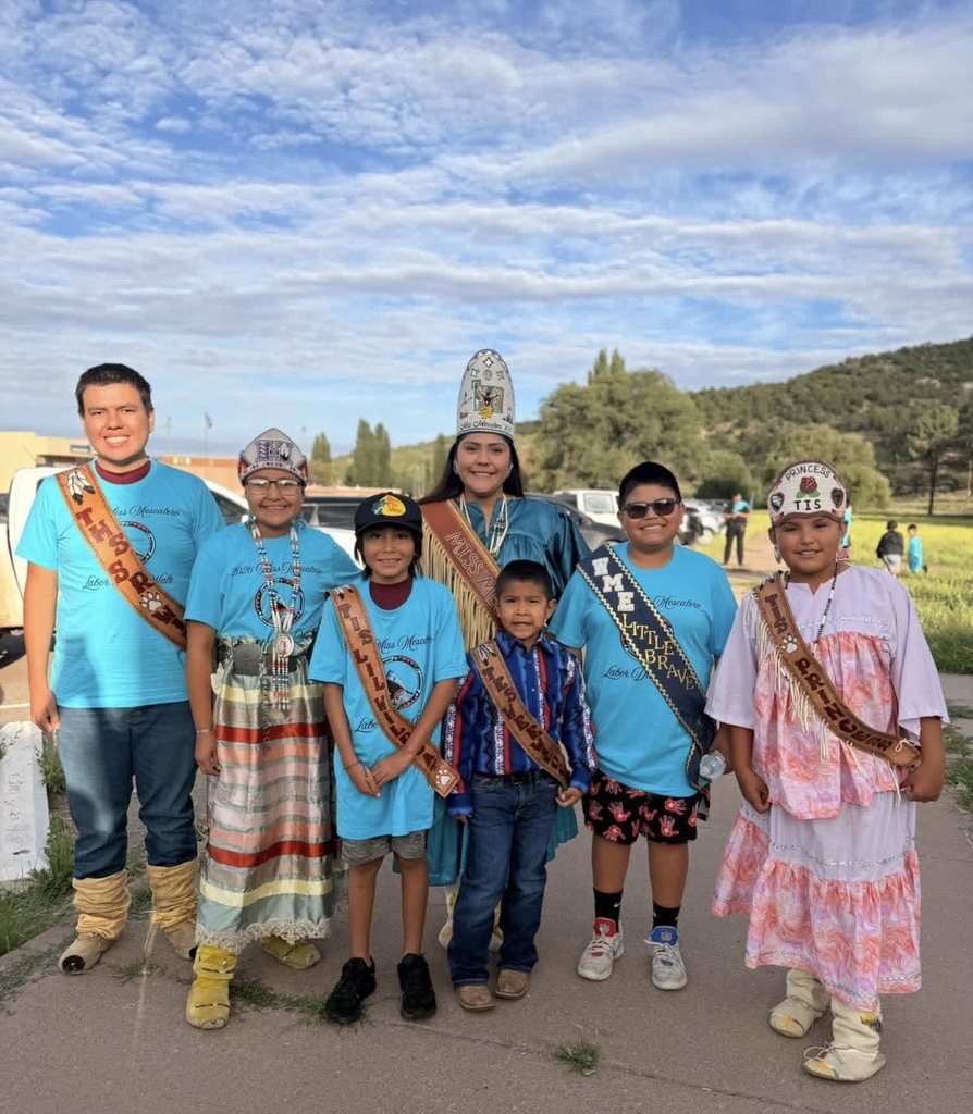 A group of people, some in traditional attire and others in blue t-shirts, stand on a path.