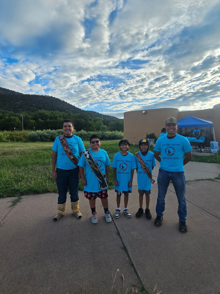 Five people wearing blue t-shirts and hats stand outside with mountains in the background.