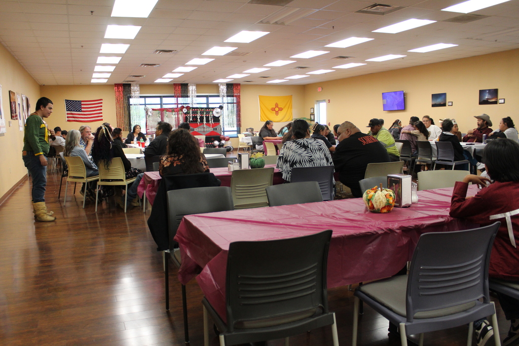 Group of people seated at tables in a dining area. A man stands near the wall.