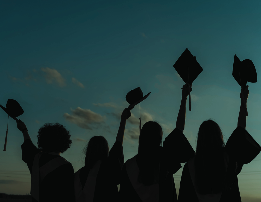 students holding their graduation caps above their heads in a sunset