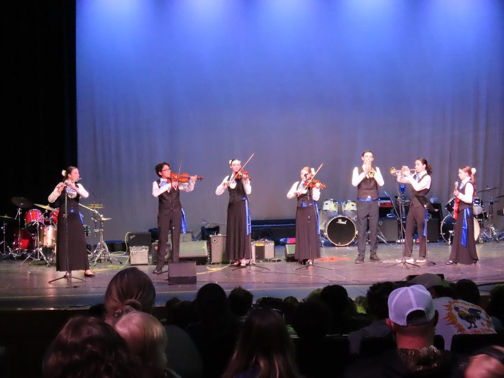 Students playing string and wind instruments on stage for battle of the bands at TFHS.