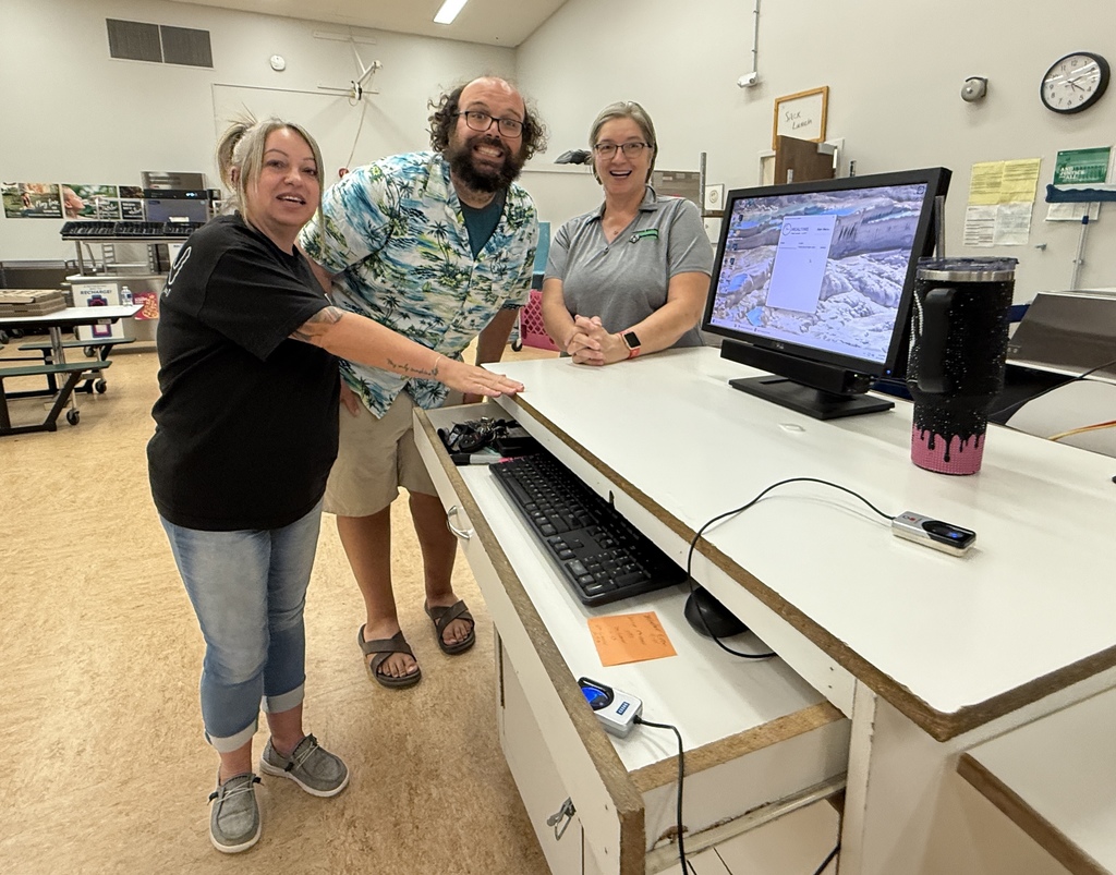 Staff members in the cafeteria standing next to a computer.