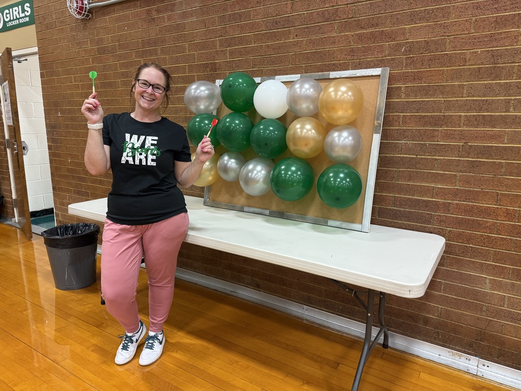 A parent with pink pants and a black shirt standing in front of a balloon game in the gym.