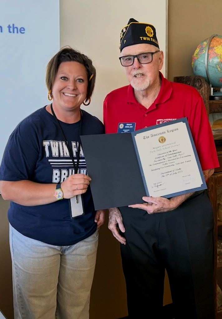 Teacher receiving an award from a man in a red shirt and a hat on.