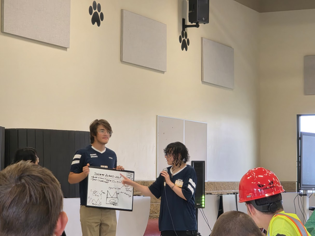 Two students stand with a whiteboard explaining to an audience.
