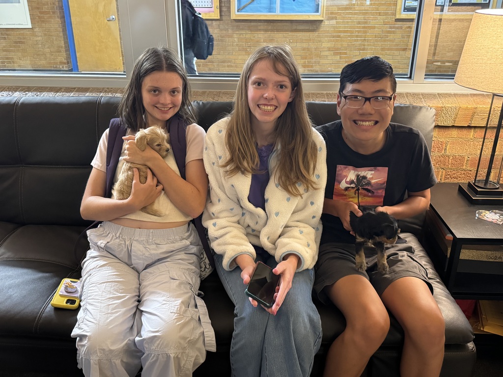 Three students sit on a couch, smiling, while holding puppies