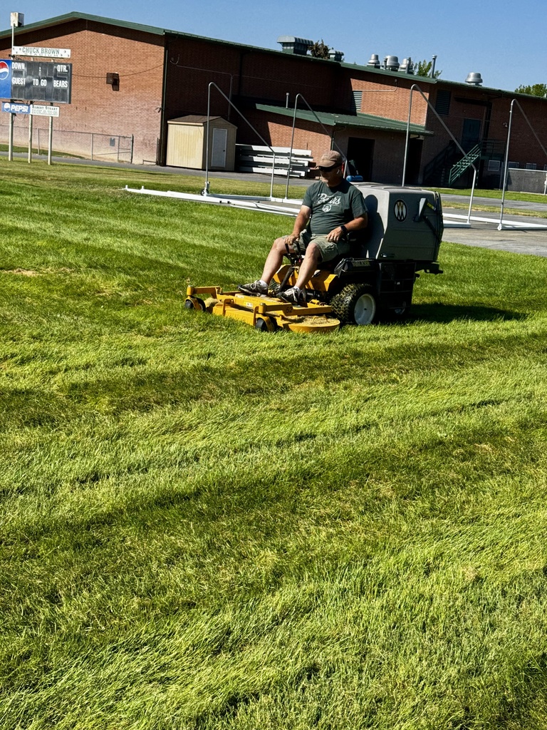 A picture of a staff member on a riding lawn mower mowing a field at school.