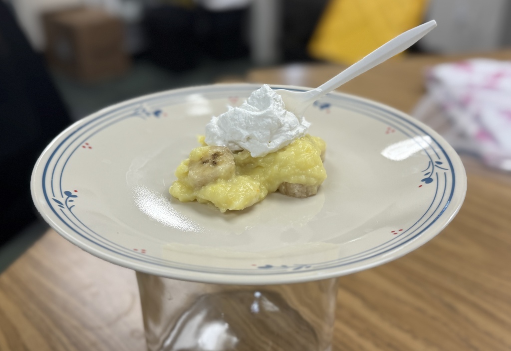 A picture of a dinner plate with a slice of banana pudding pie on it with a white fork.