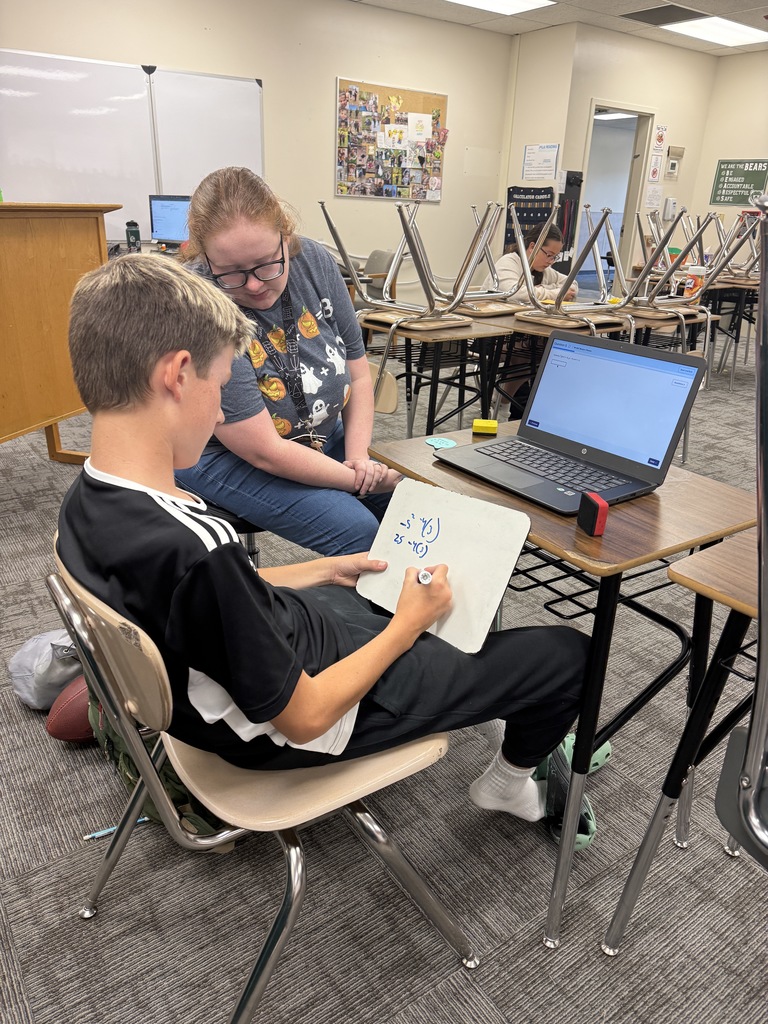 A picture of a teacher helping a student in a classroom with math work.
