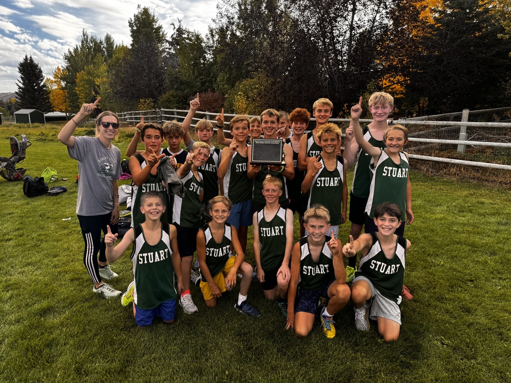 A group picture of our cross country team on a green field with a white fence behind them.