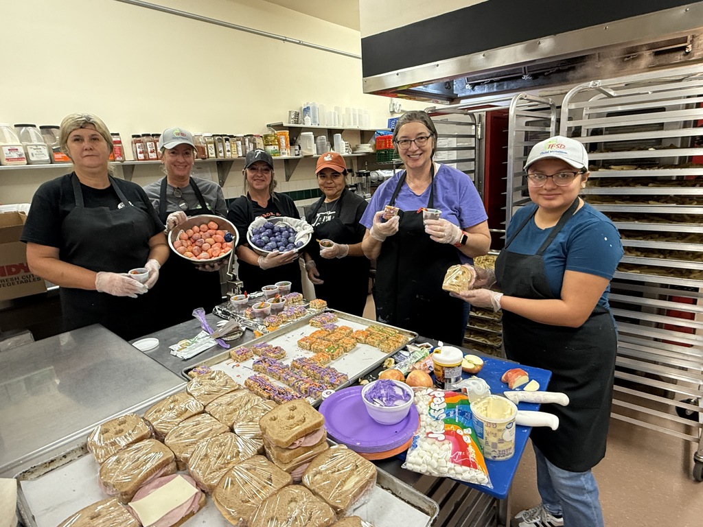 a picture of six lunch ladies in the school kitchen holding samples of lunch items on Halloween