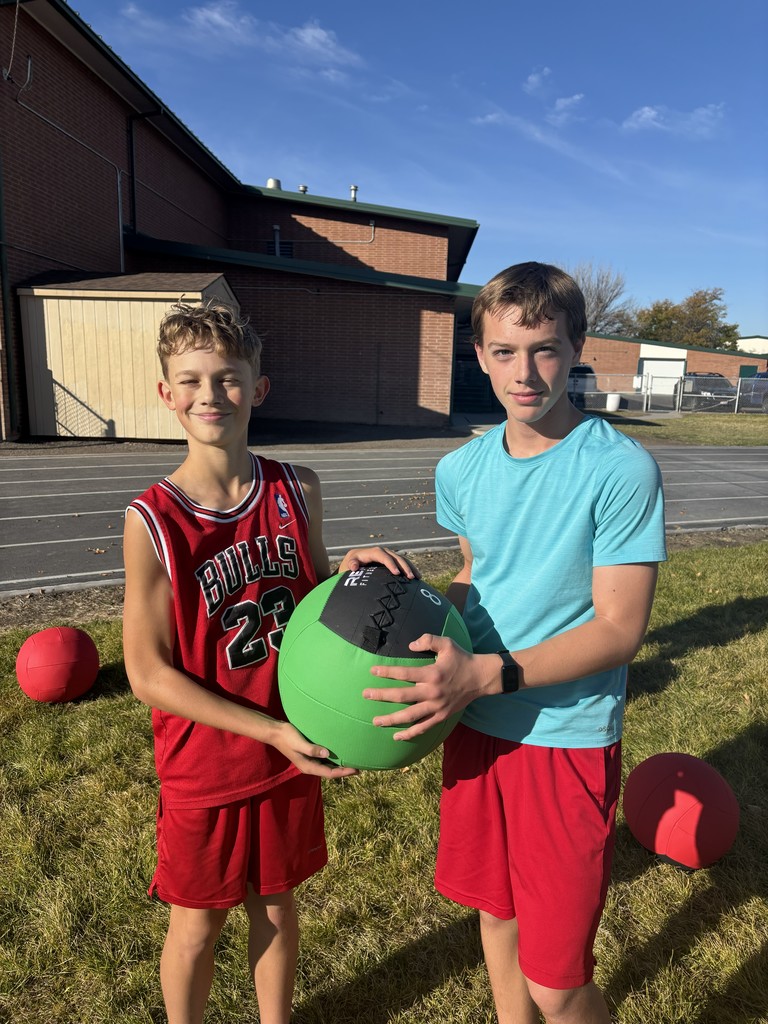 a picture of two male students outside on the school's track holding a green medicine ball