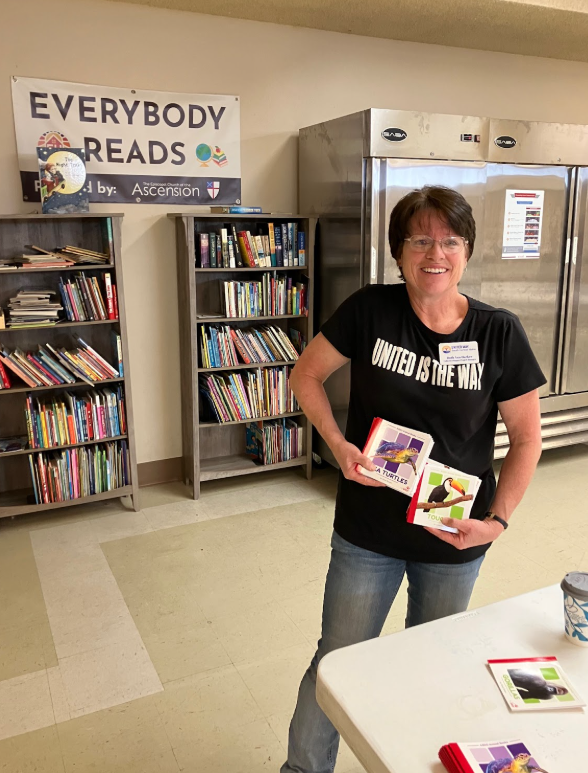 Adult in a United Way t-shirt holding children's books.