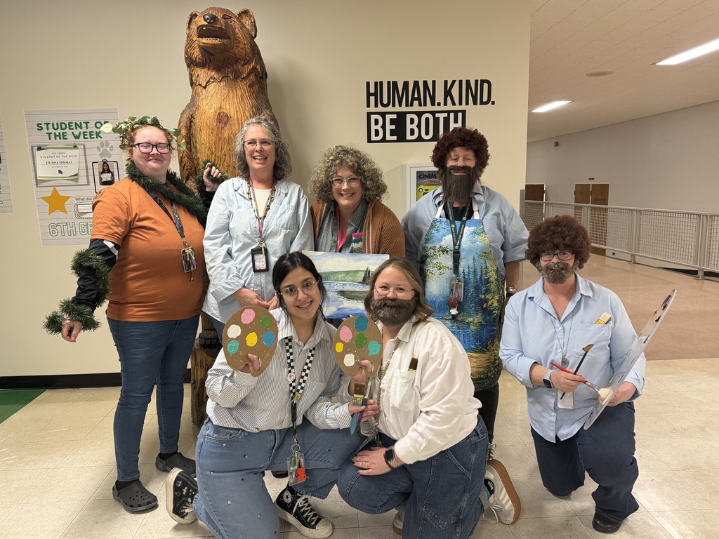 a picture of a group of teachers dressed as artist Bob Ross and standing in front of a carved wooden bear