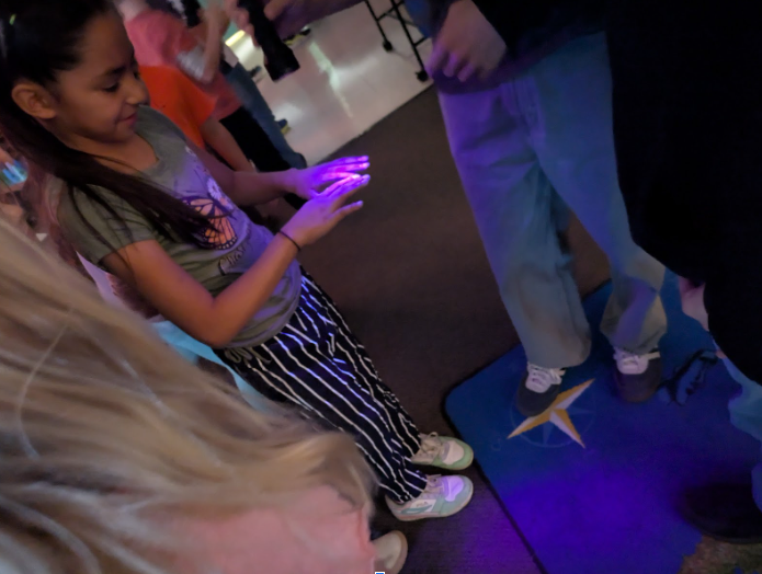 Student inspecting child's hands with purple light
