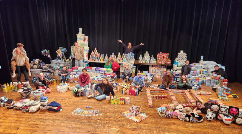 Students posed and smiling throughout an entire stage full of donations that have been sorted.