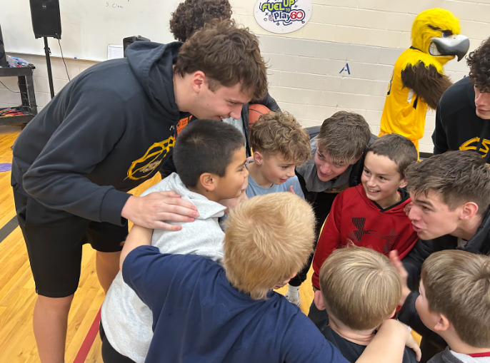 3 CSI students huddled up with  an  excited group of elementary aged boys.