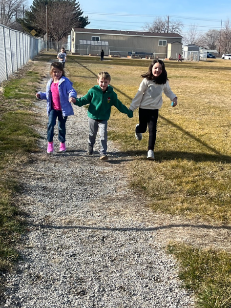Three kids walking along a path holding hands and smiling.