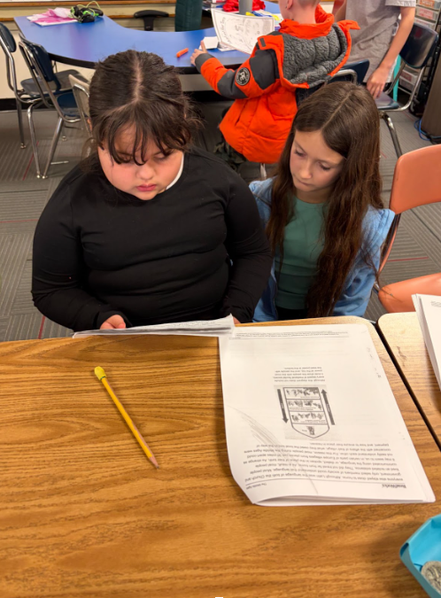 Two students sitting at a desk looking over a packet.