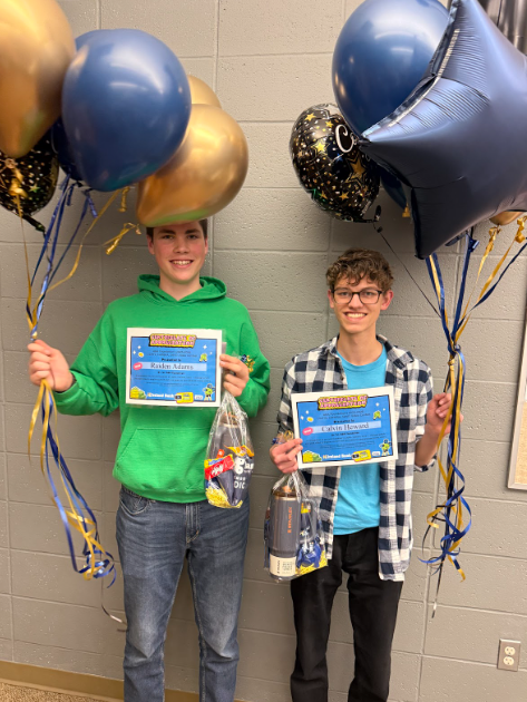 2 students each holding balloons, certificates, and goodie bags full of prizes.