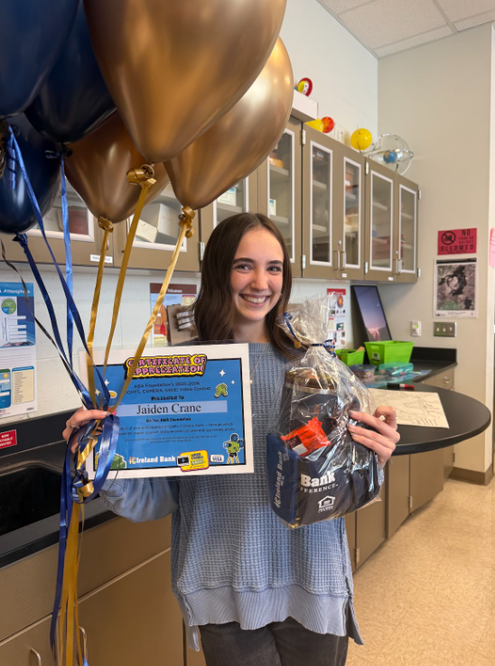 Student poses with balloons, certificate, and goodie bag full of prizes.