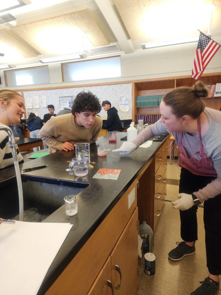 Students peering into a beaker sitting on a counter top in science classroom as the pink contents of the beaker fizz up