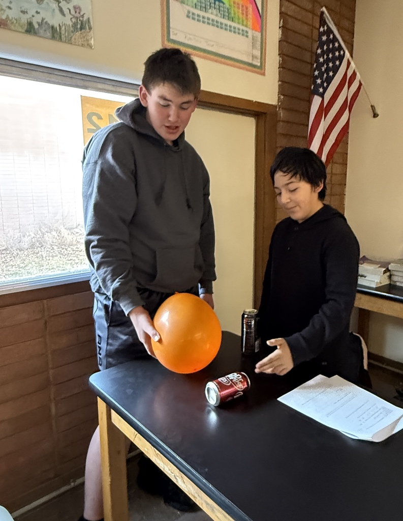 Two male students with a ballon and a pop can on a black table conducting an experiment.