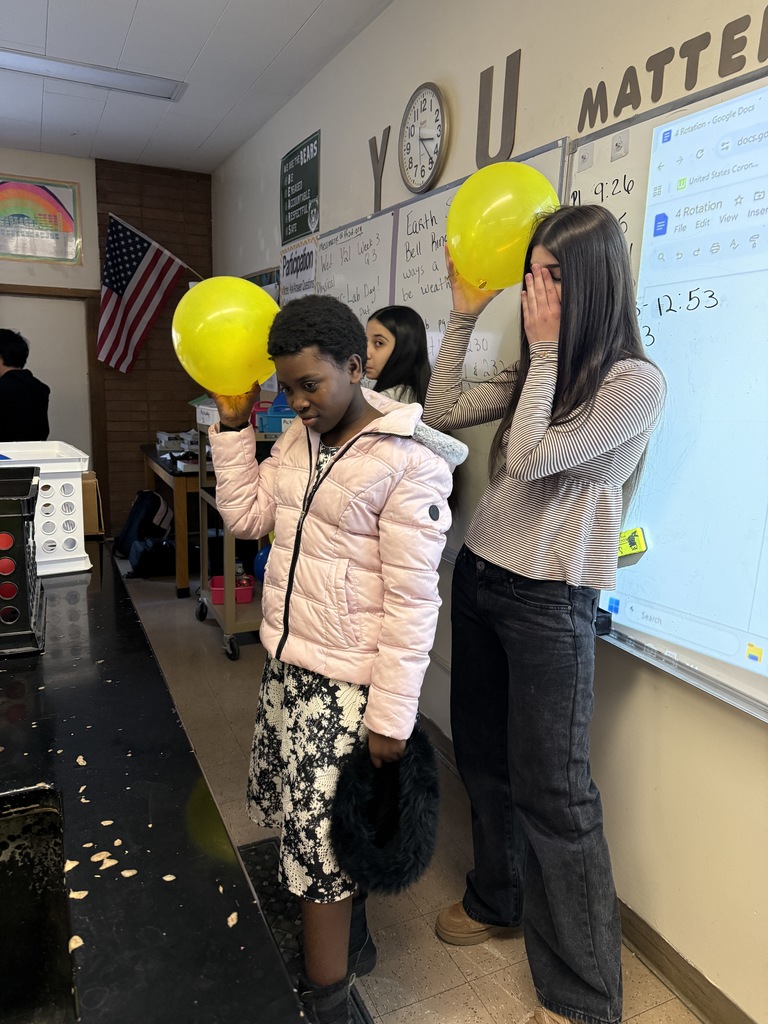 Two female students with rubbing yellow balloons on their heads in class.