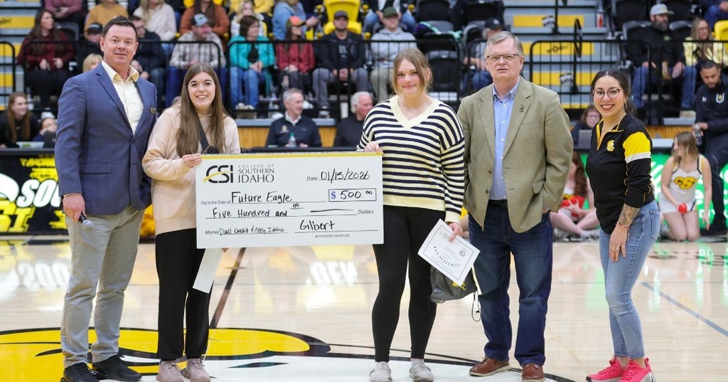 Two students and 3 adults standing center court, with the two students hold each end of a giant check 