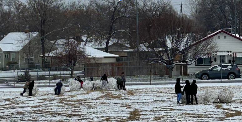 Students  in the  field on playground pushing boulders of snow that are almost as big as they are.