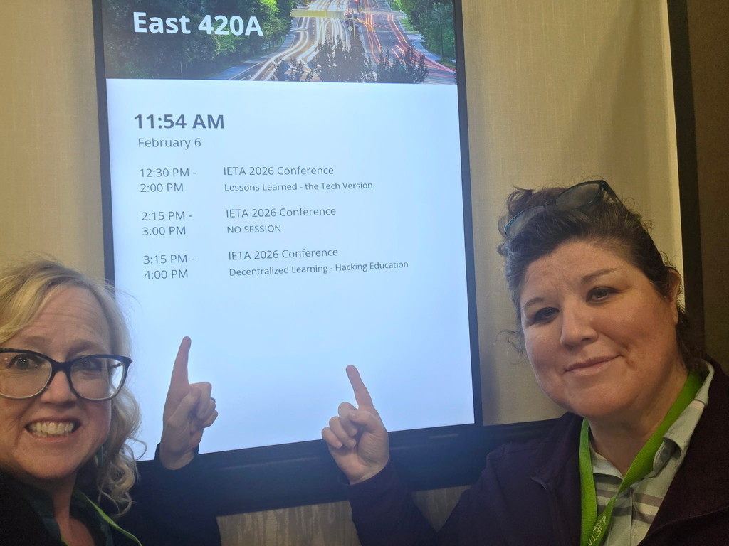 Two women point to a screen with a schedule for a conference