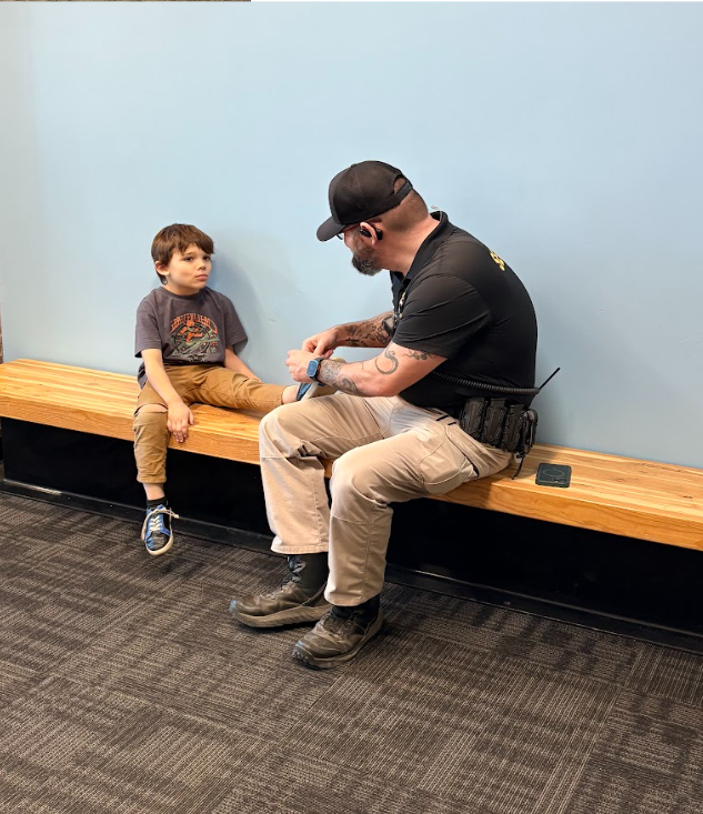 School security officer sitting on a bench with a student tying his shoe.
