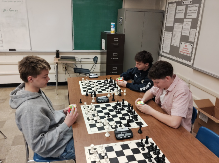 3 students sitting at a table with chess boards on it