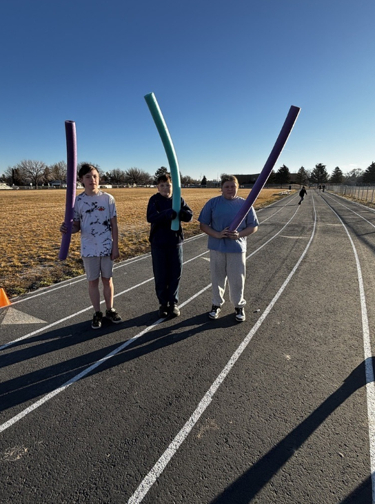 three students on the track with pool noodle "torches"