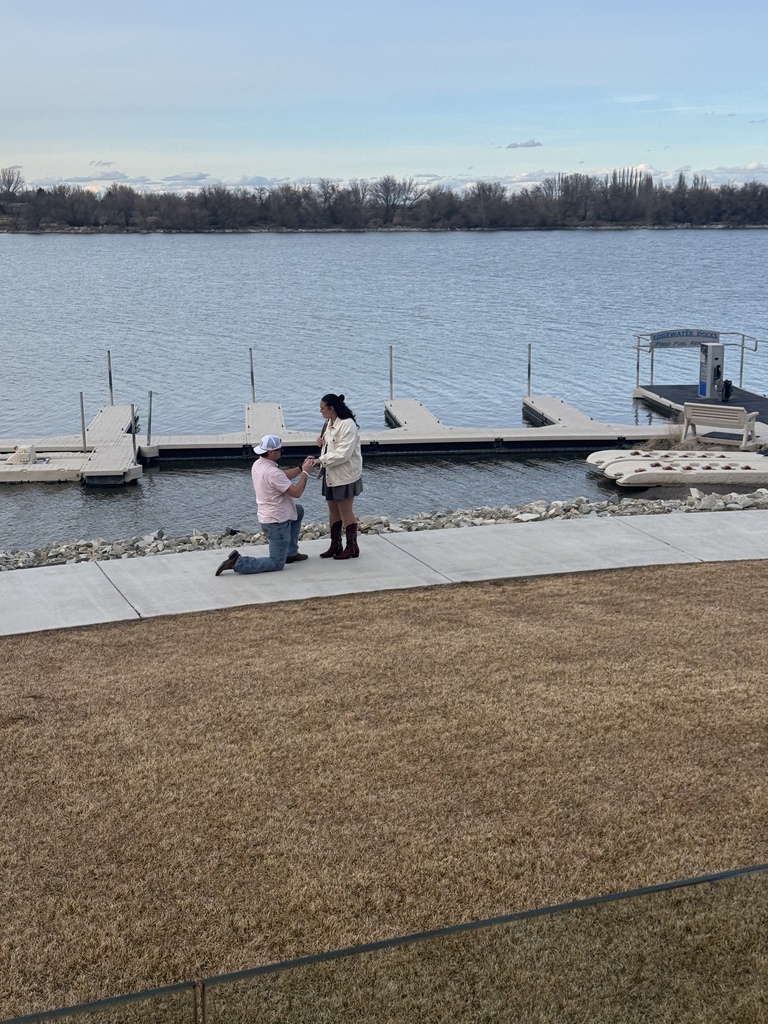 A man on one knee proposing to his then girlfriend, now fiancée with the river as a beautiful backdrop 