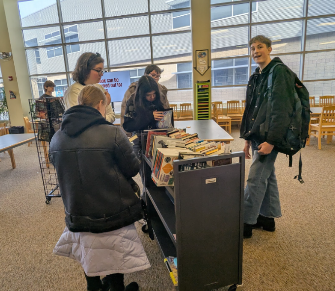 Students browsing through a rolling bookshelf filled with books
