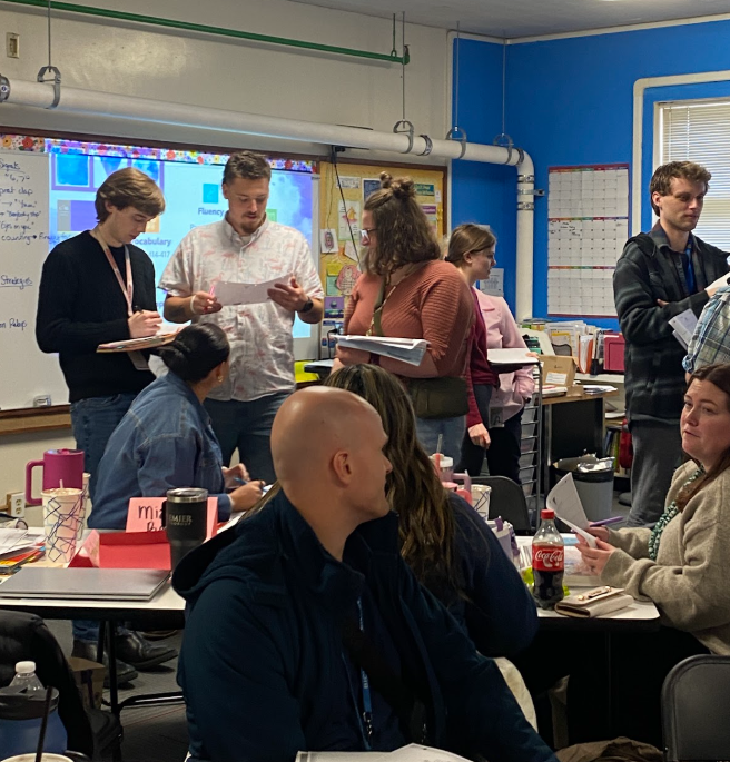 Teachers, senior and novice, meandering around a classroom engaged in an activity together