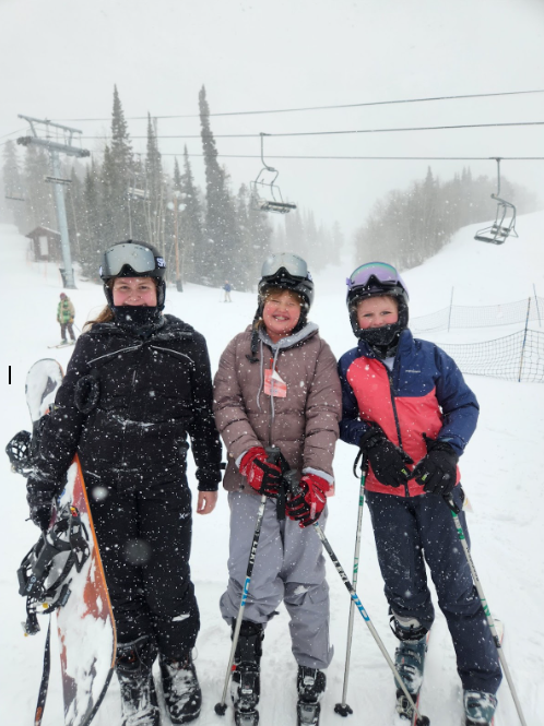 Students all geared up to ski standing in front of a ski lift while snow is falling