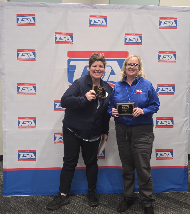 Two women hold plaques after winning award, standing in front of TSA backdrop.