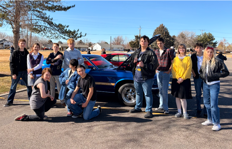 Students dressed in their best "Outsiders" attire surrounding a vintage car with the hood up