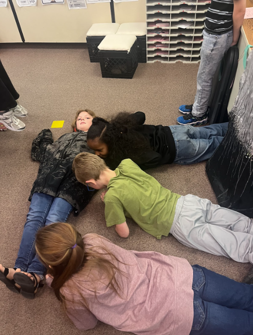 Four students laying down making the letter "E"