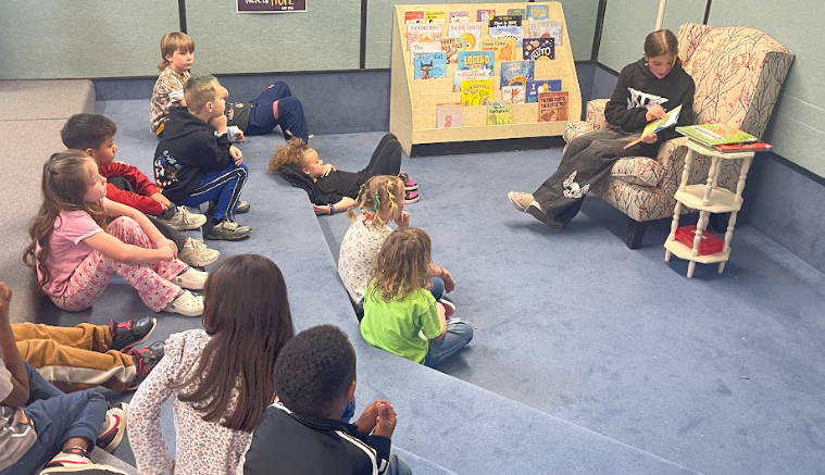 Student reading a book to other students