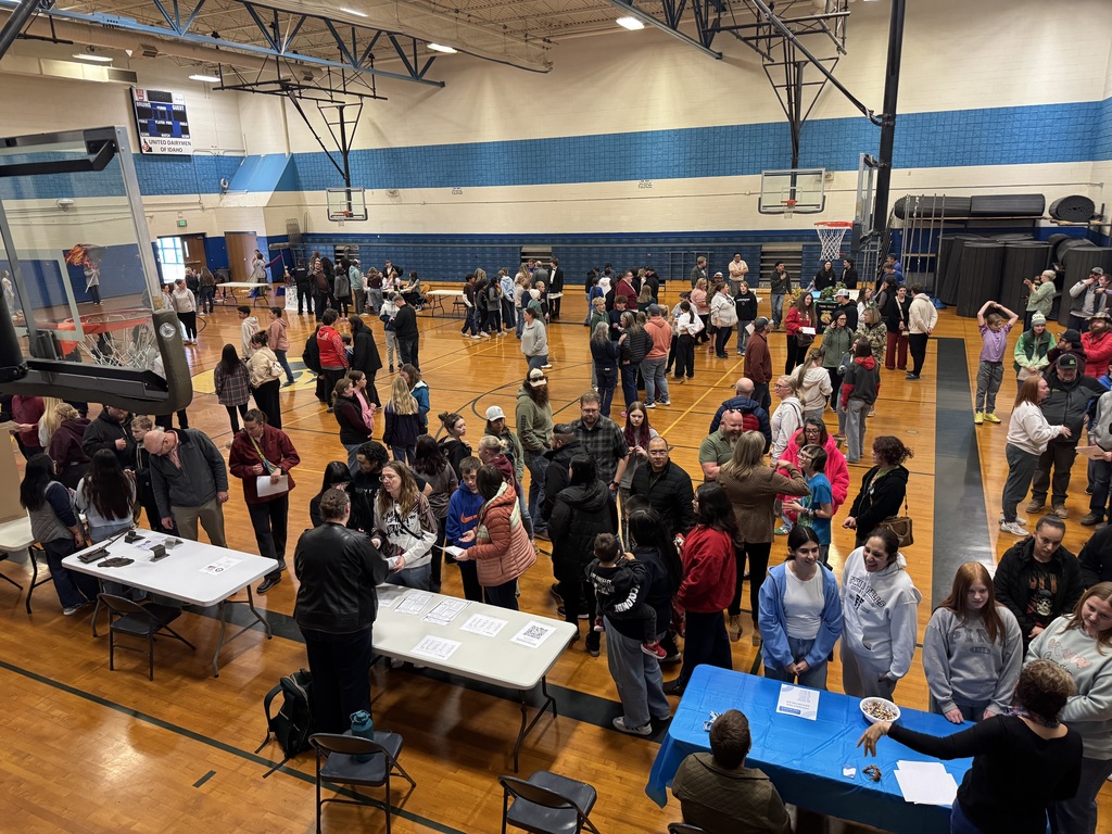 Gym full of students and parents talking to teachers at tables.