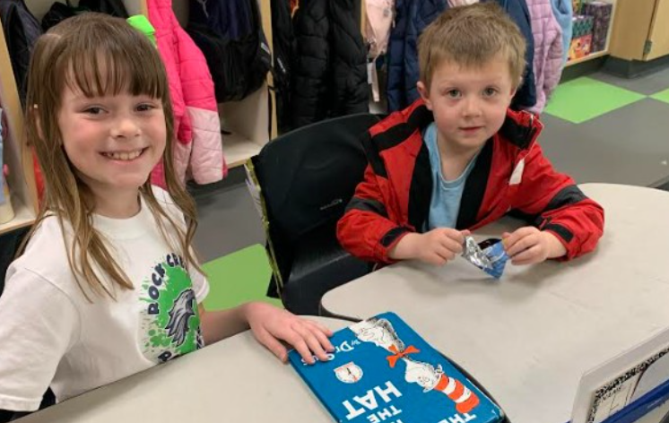 Two students sitting together, smiling with a book