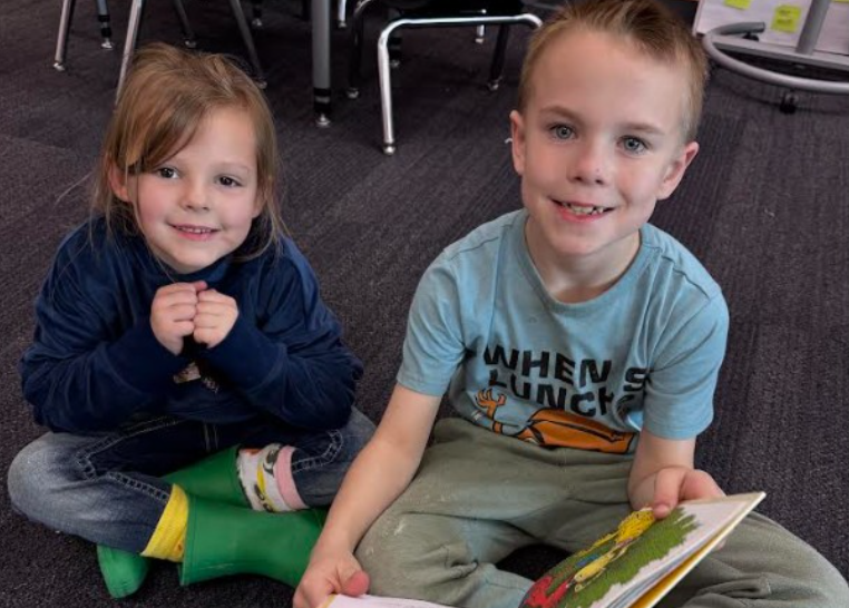 Two students sitting together, smiling with a book