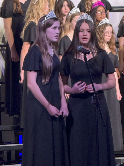 Two girls wearing tiaras and standing in front of a microphone singing