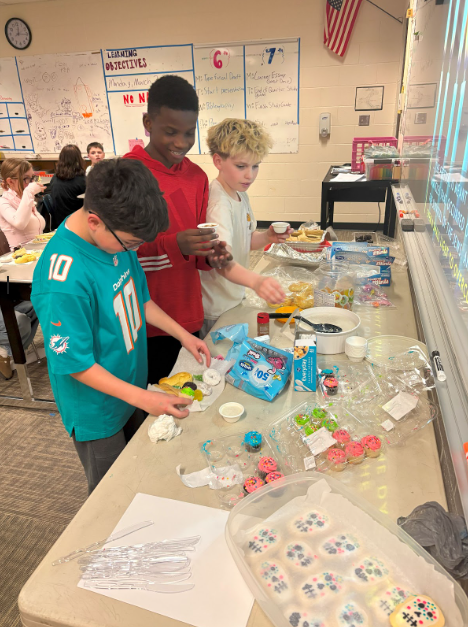 Three boys standing along a table filled with an array of homemade treats
