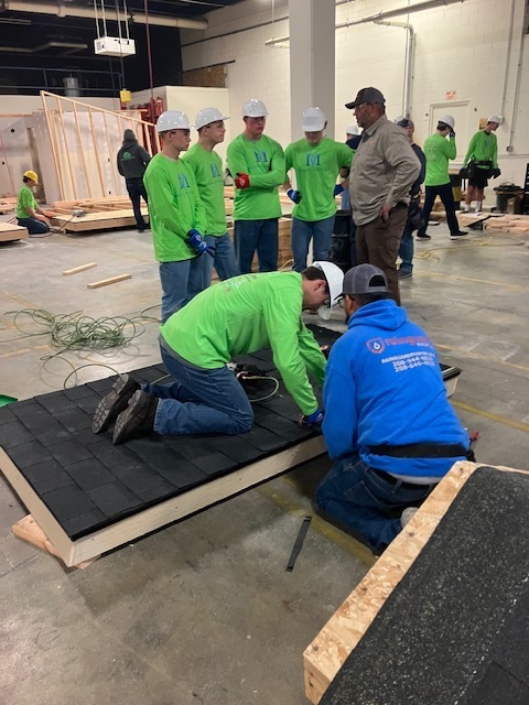 A student working on a false roof while four others listen to an instructor intently.